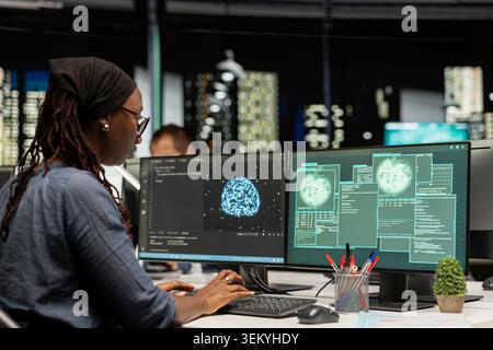Software developer at office desk doing maintenance on computer systems using AI. African american woman in tech startup preventing issues bug affecting server networks using artificial intelligence Stock Photo