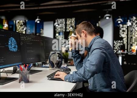 Tired man drinks coffee while utilizing AI on computer to optimize performance. Exhausted worker enjoys caffeinated beverage in tech company office while training deep learning models Stock Photo
