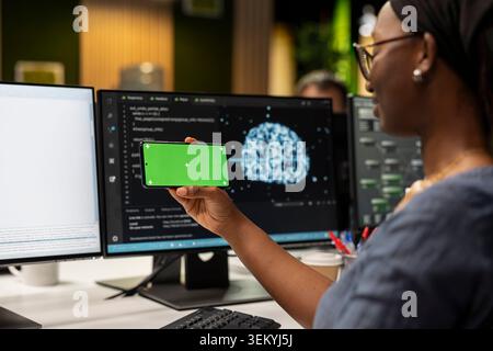 Engineer in tech startup office developing apps using AI automation on isolated screen smartphone. Worker debugging applications with artificial intelligence on mockup mobile phone Stock Photo