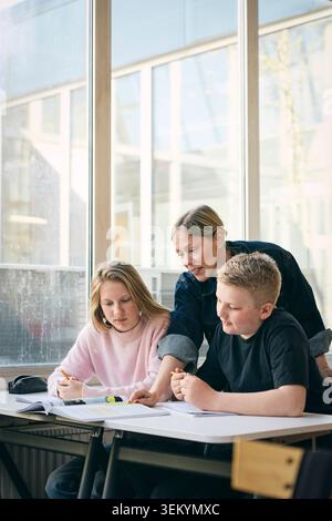 Female teacher guiding students with studies in classroom at junior high school Stock Photo