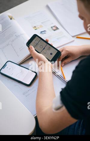 Over the shoulder view of boy checking blood sugar level while sitting at desk with books in classroom Stock Photo
