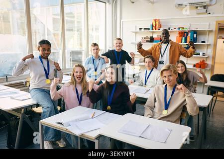 Portrait of junior high students wearing medals showing winning fist with teacher in classroom at school Stock Photo