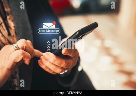New Message Notification Icon Floating over Smartphone Held by Woman. Email marketing, online communication, instant messaging, and social media. Stock Photo
