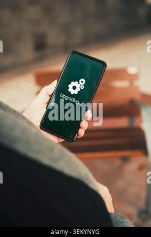 Smartphone Upgrading System Update Held by Woman Outdoors. Software updates, system maintenance, mobile technology, and app upgrades. Stock Photo