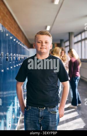 Portrait of confident junior high male boy standing near lockers in school lobby Stock Photo