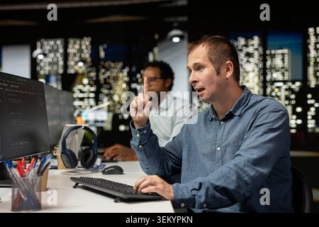 Upset engineer raising complains in startup office, noticing error in code while doing quality assurance. IT professional raising finger, concerned by mistakes in programming language on computer Stock Photo