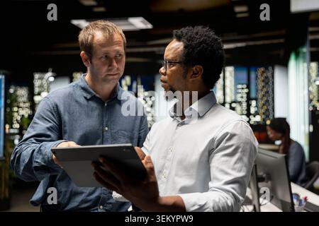 Team of engineers use tablet in tech startup office to develop apps using AI automation. Teamworking colleagues working on device, debugging applications with artificial intelligence Stock Photo