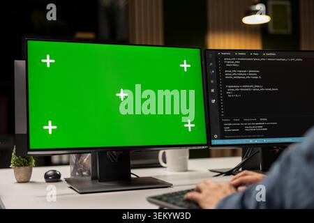 Engineer writing code on green screen PC, developing machine learning APIs. IT professional troubleshooting software errors using chroma key computer, resolving system crashes Stock Photo