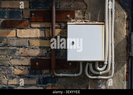 Electrical Junction Box Installed on an Aged Brick Wall Surrounded by Conduits and Metal Fixtures, Showcasing Urban Infrastructure and Maintenance Det Stock Photo