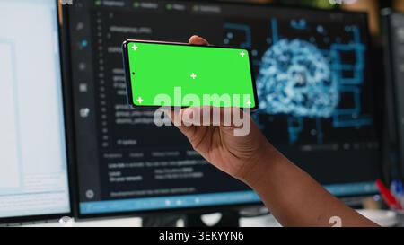 Isolated screen smartphone used by admin in office working to fix bugs in artificial intelligence system. Employee in tech startup using chroma key mockup mobile phone to watch videos Stock Photo