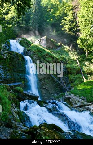 Waterfalls cascading down a lush green mountain with a small building nestled on the slope Stock Photo