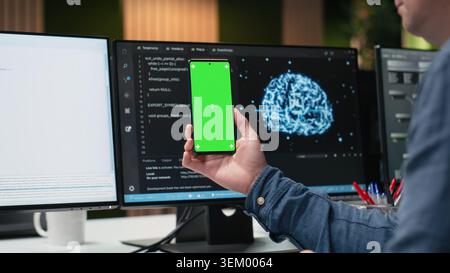 Green screen smartphone used by programmer in tech startup office developing apps. IT specialist creating applications for chroma key mobile phone, debugging glitches, close up Stock Photo