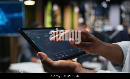 Close up of programmer typing code on touchscreen device, developing machine learning models to automate tasks in workspace. Developer checking app programming language scripts on tablet Stock Photo