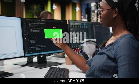 Green screen phone used by woman in company workplace doing tech quality assurance. Woman in office watches tutorial on programming languages with chroma key smartphone Stock Photo
