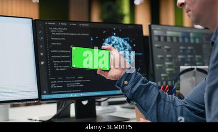 Green screen smartphone used by engineer in Silicon Valley company office developing apps. IT expert creating videogames on chroma key phone, debugging issues, close up Stock Photo