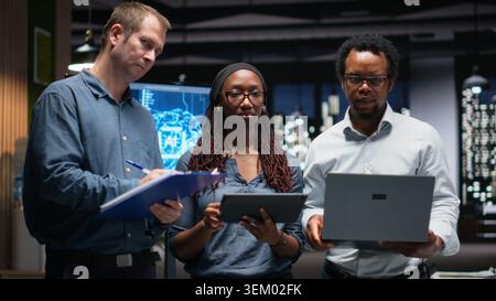 Portrait of engineering team developing artificial intelligence algorithms in high rise office. Teamworking colleagues debug 3D neural network brain models shown on screen Stock Photo