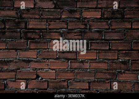 Close-up of a dark red brick wall with deeply ridged surfaces and rough grey mortar joints, forming a bold repeating pattern. Stock Photo