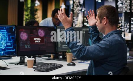 Upset programmer at office desk thinking how to fix critical error alert displayed on PC screen. Tech agency IT expert annoyed by computer bug affecting server network, brainstorming solutions Stock Photo