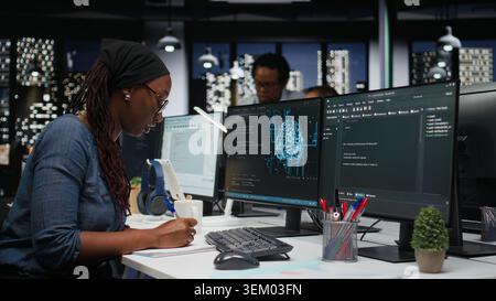 Software developer in office writing on notepad, working to fix bugs in artificial intelligence system. IT expert taking notes at desk, troubleshooting neural network errors in tech startup Stock Photo