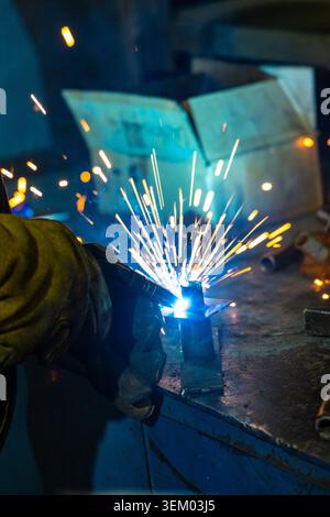 Industrial welder working with metal and bright welding sparks in workshop Stock Photo