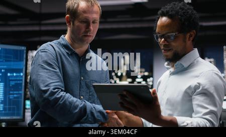 Engineering team using tablet in office, working with AI programming languages. Teamworking colleagues using device in company workplace to do artificial intelligence tech quality assurance Stock Photo
