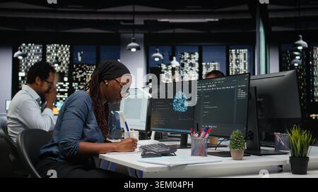 Programmer taking notes at desk in Silicon Valley company office, developing apps. IT expert using machine learning to do coding, writing on notepad, debugging applications to resolve issues Stock Photo