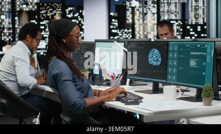 Female programmer using large language model application to get help with coding tasks. African american woman interacting with AI LLM chatbot PC GPT software on PC Stock Photo