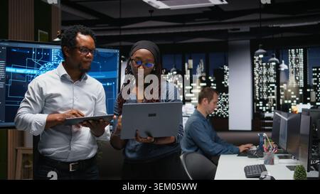 Tech agency colleagues collaborating to optimize AI performance in office late at night. Software developers use machine learning on devices for debugging, analyzing code Stock Photo