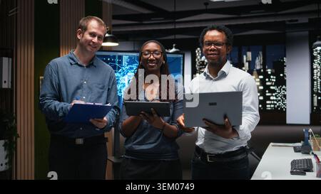 Portrait of smiling tech startup colleagues brainstorming ways to optimize performance in office. Happy programmers use devices for debugging, typing lines of code Stock Photo