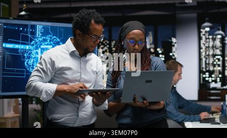 Tech agency colleagues collaborating to optimize AI performance in office late at night. Software developers use machine learning on devices for debugging, analyzing code Stock Photo