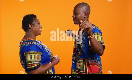 African american partners having fun dancing in studio, enjoying their favorite song and showing romantic slow dance moves. Ethnic married couple listening to cool songs over orange background. Stock Photo