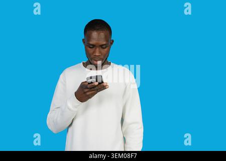 Young black man concentrating on smartphone content, isolated on blue background Stock Photo