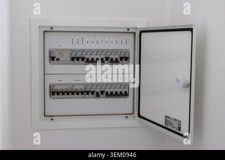 A modern electrical distribution board with multiple rows of circuit breakers and labeled circuits, its white door is ajar revealing a tidy internal s Stock Photo