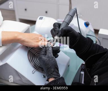 Professional hardware manicure process Caucasian master hands in black gloves Stock Photo