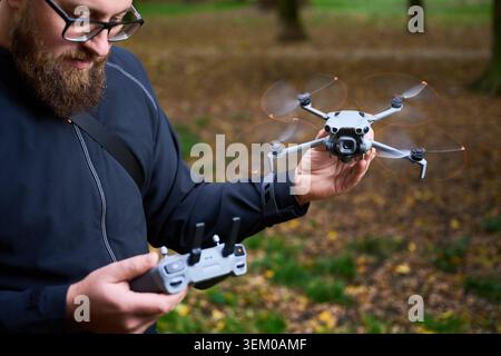 Man holds flying drone and controls it with remote. Bearded man operating quadcopter in a park, testing equipment for aerial photography, concept of modern technology and hobby Stock Photo