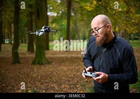 Man controlling flying drone. Bearded man operating quadcopter in park, focused on flight and reacting with excitement, concept of modern technology and hobby Stock Photo