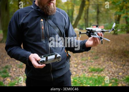 Man holds drone and controller, preparing for takeoff. Bearded man setting up quadcopter in a park, checking equipment for aerial photography and filming, concept of modern technology and hobby Stock Photo