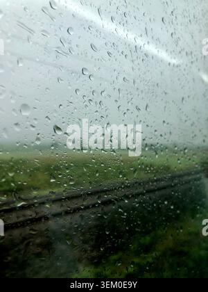 Rain drops on glass window. View from a tunning train on a rainy day showing rail tracks and green scenery. Stock Photo