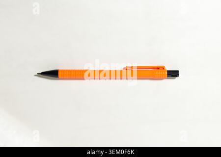 Orange mechanical pencil lies horizontally on white background. Black tip and clip highlight details. Textured grip enhances usability. High quality photo Stock Photo