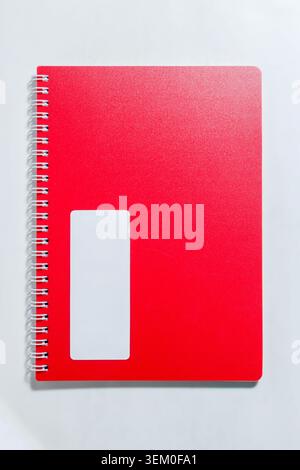 Bright red notebook cover features smooth texture. White rectangular label appears on the front. Silver spiral binding holds the notebook securely. High quality photo Stock Photo