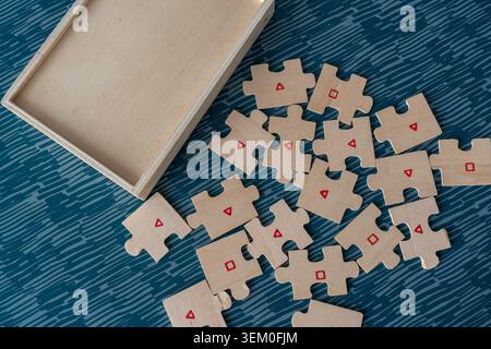 Wooden puzzle pieces with red triangle and square symbols spread next to open wooden box top view. Concept of cognitive play, shape learning and Stock Photo