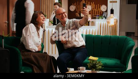 Older guests using videocall connection to keep in touch with family back home, travelling on retirement holiday. Husband and wife talking to children and nephews on teleconference call. Stock Photo
