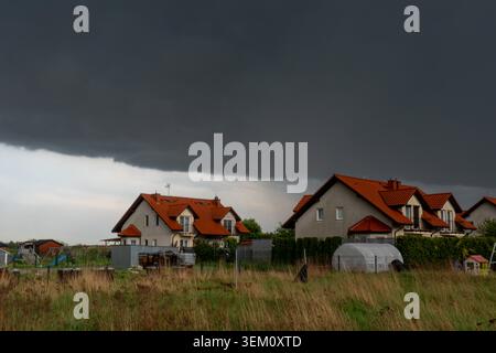 Heavy rain clouds gathering above suburban neighborhood with houses and gardens before summer storm. Concept of unsettled weather, seasonal changes Stock Photo