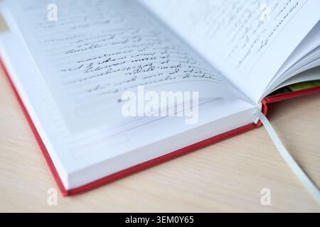 Open Red Bound Notebook With Handwritten Cursive Entries On Lined Pages Lying On Wooden Desk, Ribbon Bookmark Visible, Shallow Depth Of Field And Indoor Daylight Writing Study Scene. Stock Photo