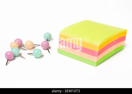 Perspective view horizontal closeup of square multi colored sticky note block with heap of pastel push pins on white copy space background Stock Photo
