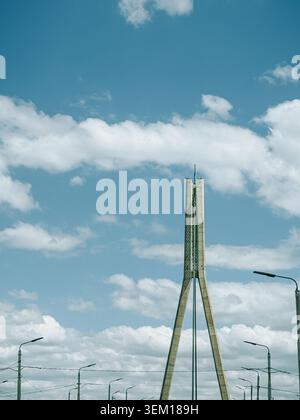 Riga, Latvia - June 4, 2026: Minimalist view of a cable-stayed bridge pylon rising beneath a vast blue sky with scattered clouds. Modern transportatio Stock Photo