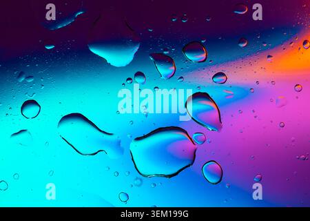 Macro shot of fluid dynamics showing floating oil drops over vibrant, colorful light leaks Stock Photo