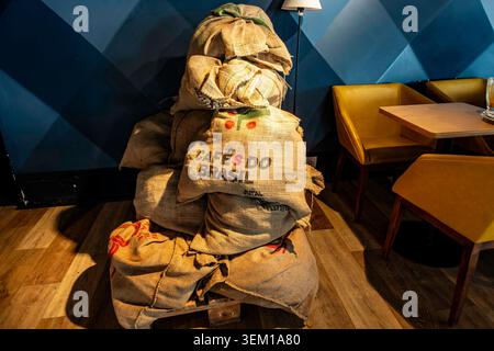 A stack of burlap coffee sacks reading "Cafés do Brasil" on a wooden pallet inside a modern café with yellow chairs in Durrës, Albania. Stock Photo