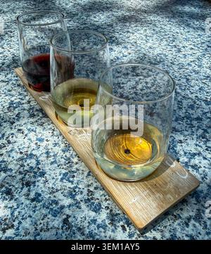 Three wine samples served in stemless wine glasses on a rustic wooden board atop a blue granite tabletop. Stock Photo