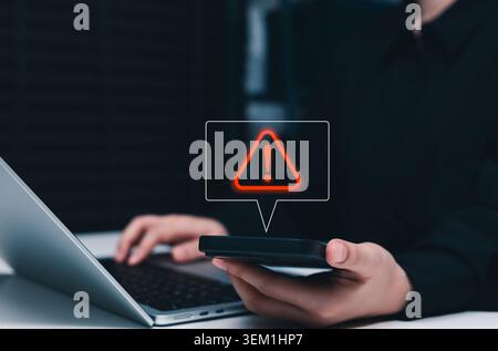 Cybersecurity warning alert and cyber risk notification concept. Person using smart phone and laptop, red danger icon, account threat, fraud detection Stock Photo